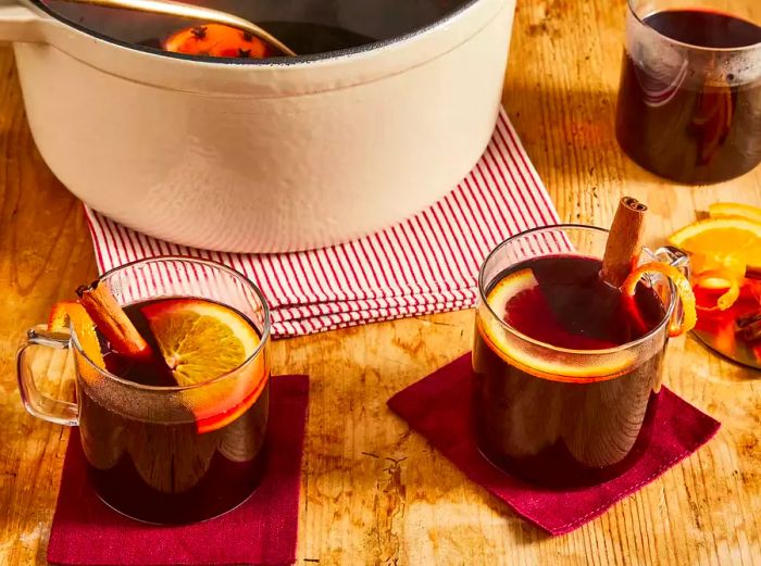 Three clear mugs of spiced wine, each topped with orange slices and cinnamon sticks.