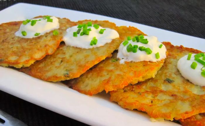 Latkes topped with sour cream and chopped chives, served on a rectangular platter