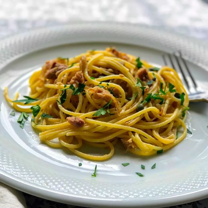 A top-down view of a plate of spaghetti with tuna and capers