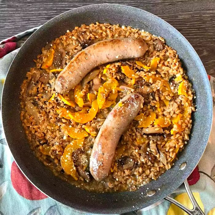 A bird's-eye view of a skillet filled with sausage, farro, mushrooms, and delicata squash