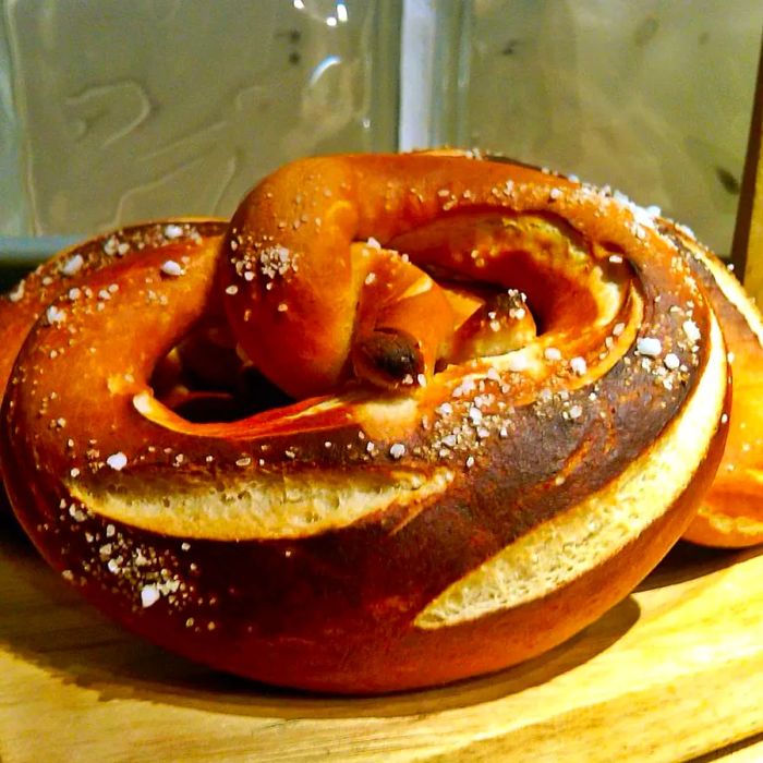 A close-up of a dark brown, soft pretzel on a wooden surface