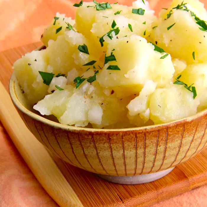 A bowl of hearty potato salad made with white potatoes, garnished with fresh, chopped parsley