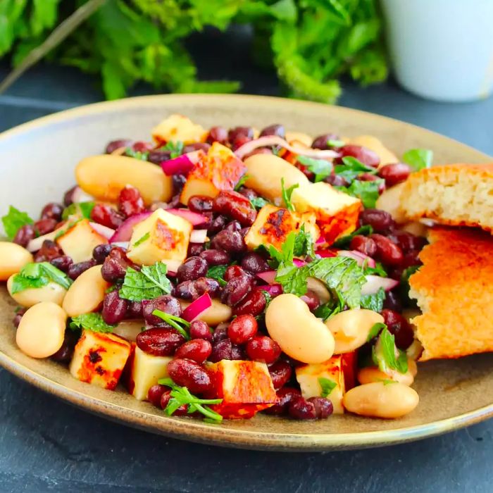 A mid-angle view of a bowl filled with halloumi three-bean salad, dressed with pomegranate harissa vinaigrette