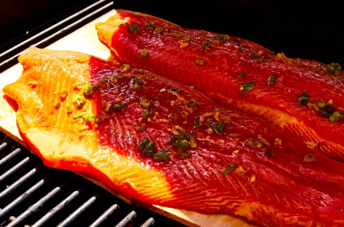 Two marinated salmon fillets placed on cedar planks on a grill