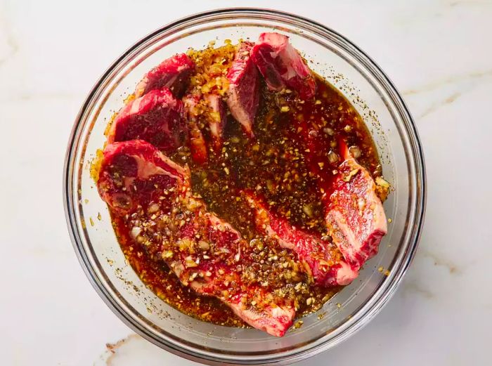 A bowl containing raw short ribs soaking in marinade