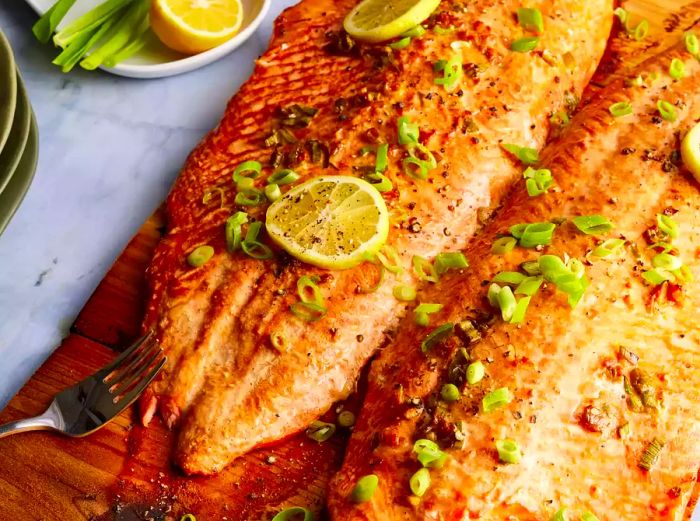 Two salmon fillets on cedar planks, garnished with sliced green onions and lemon slices