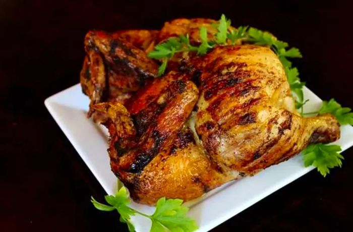 A beautifully roasted rotisserie chicken served on a white plate with fresh green garnish