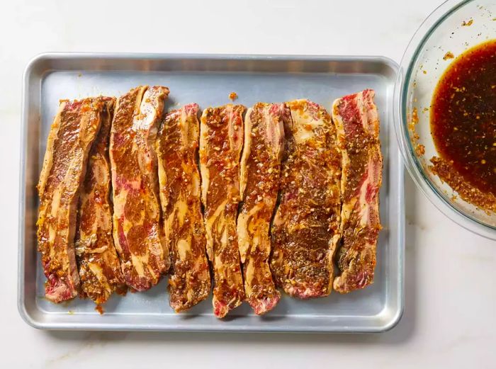 A baking tray filled with raw, marinated short ribs