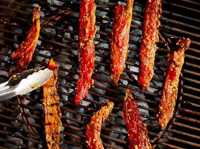 Flank steak slices grilling on the preheated grill until they achieve a slight char.