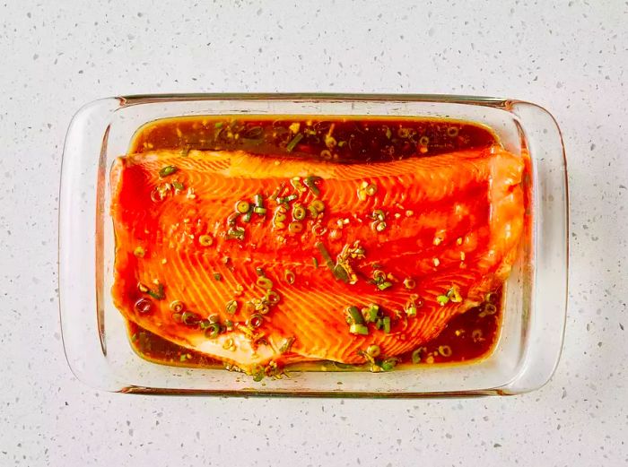 A large glass dish with two salmon fillets soaking in soy marinade