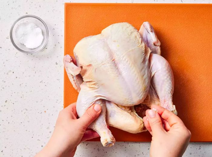 A hand sprinkling salt into the cavity of a whole chicken