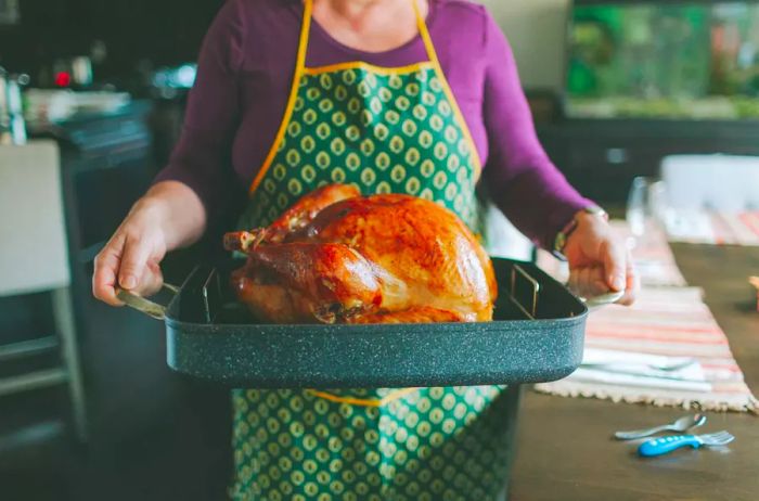 A woman carrying a tray with a perfectly roasted turkey in the kitchen