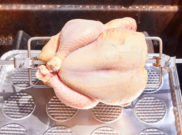 A whole chicken placed on a rotisserie attachment over a grill