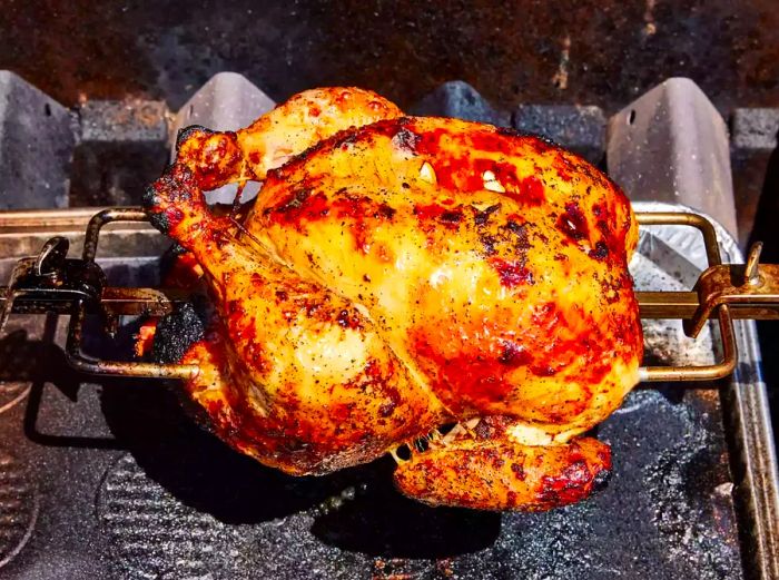 A golden-brown, cooked whole chicken on a rotisserie attachment over a grill