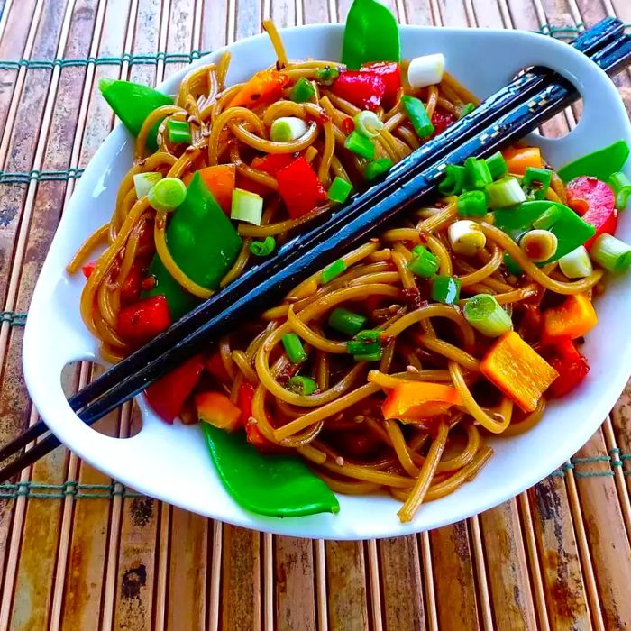 Noodles and vegetables tossed in a savory sauce, served with chopsticks