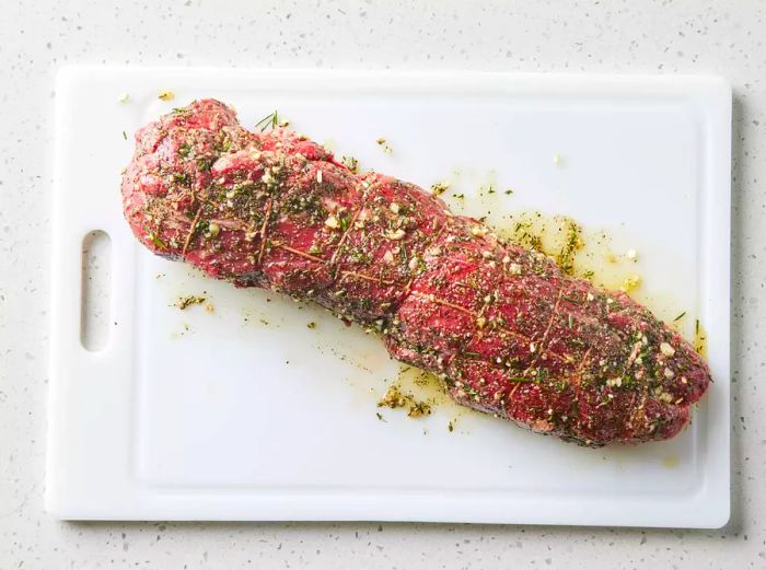 Beef tenderloin with a herb-garlic-pepper coating placed on a white cutting board.