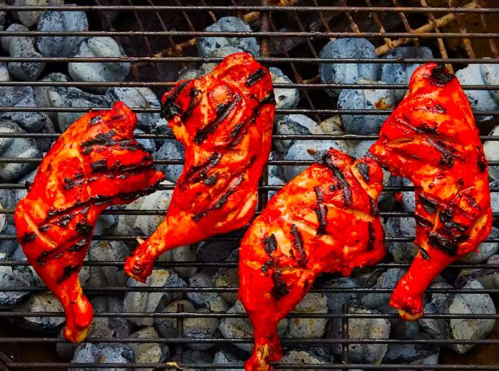 An overhead shot of tandoori-style bone-in chicken grilling on a hot barbecue.