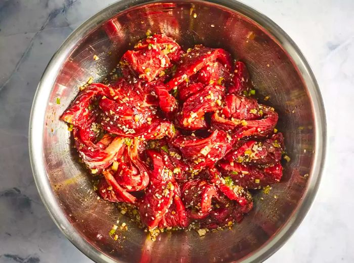 Flank steak slices placed in a shallow dish, with marinade poured over them.