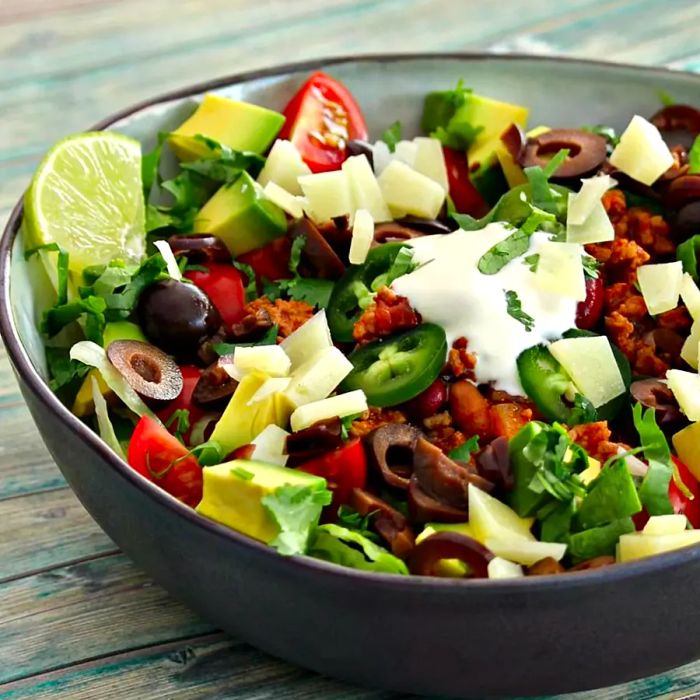 A vibrant bowl filled with seasoned ground beef, juicy tomatoes, black olives, and creamy avocado, topped with sour cream and garnished with a lime wedge