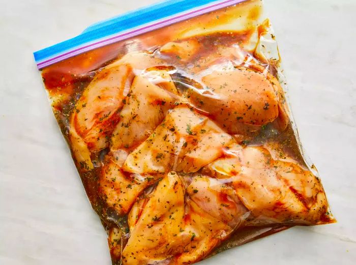 Raw chicken and marinade inside a resealable plastic bag.