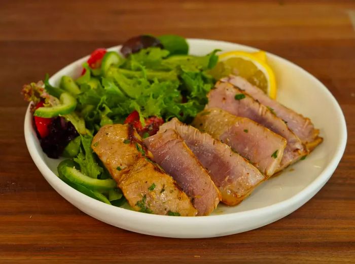 Seared tuna steaks paired with a fresh side salad and a lemon wedge, served on a white plate.