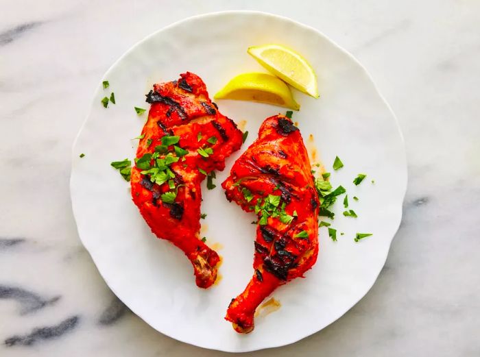 Tandoori chicken beautifully garnished with cilantro and fresh lemon wedges.