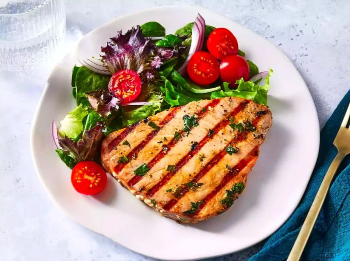 A marinated tuna steak plated with a fresh mixed green salad.