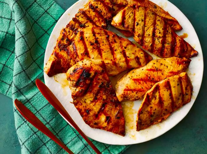 A top-down view of a plate of marinated grilled chicken resting on a green towel.