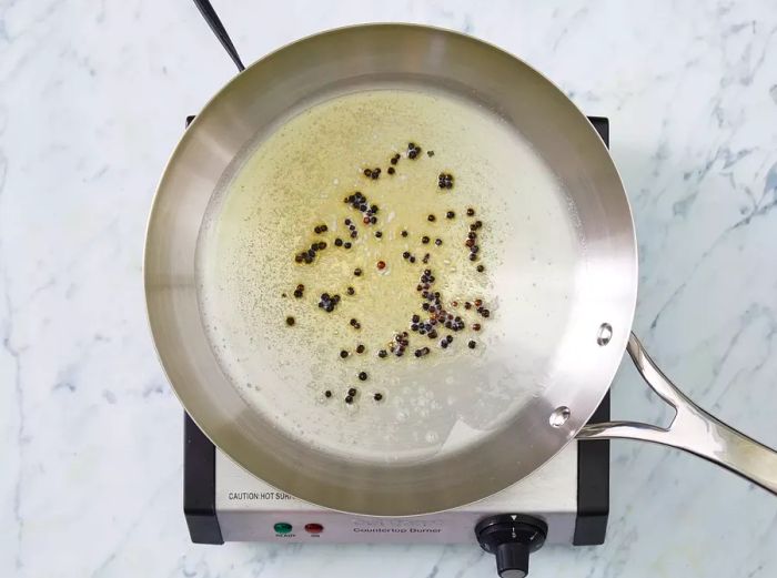 Top-down view of a pan with melted butter and peppercorns