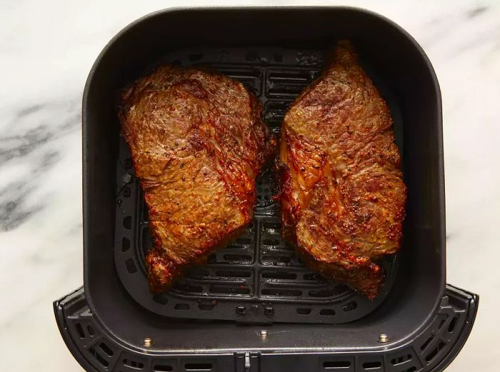 Top view of two perfectly cooked steaks in an air fryer basket.