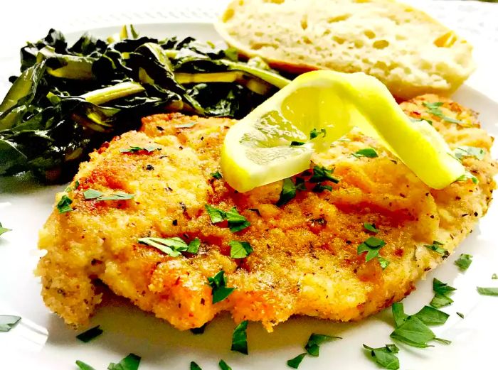 A golden, breaded chicken breast on a plate, beautifully garnished with a twist of lemon and a sprinkle of fresh parsley.