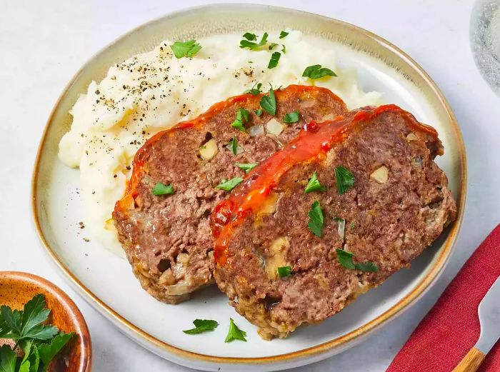 A close-up of a plate with creamy mashed potatoes, accompanied by two slices of savory meatloaf on the side.