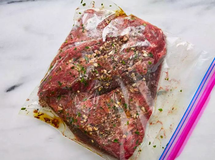 A top-down view of a resealable plastic bag with a steak marinating inside.