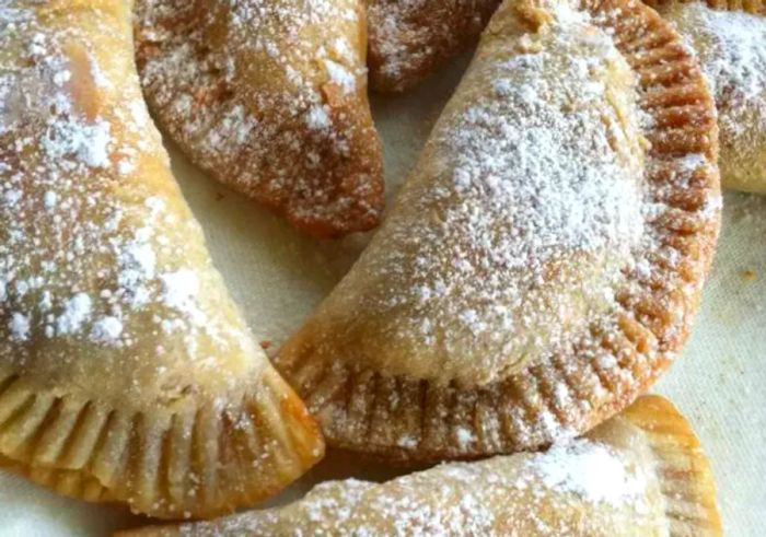 Golden fried apple pies, dusted with a light layer of powdered sugar.