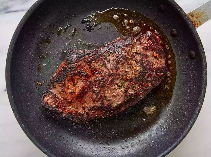 Top-down shot of a steak sizzling in a hot pan.