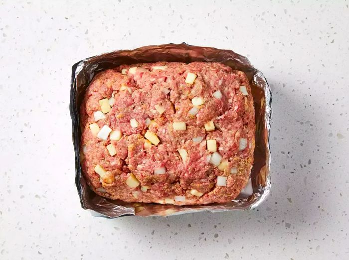 The beef mixture is molded into a loaf and surrounded by a makeshift aluminum foil pan.