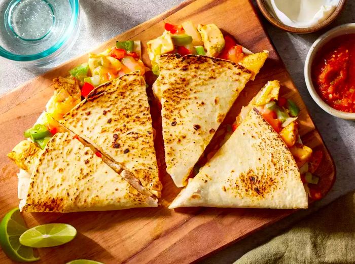 A close-up view of a chicken quesadilla, sliced into quarters and accompanied by dipping sauces.