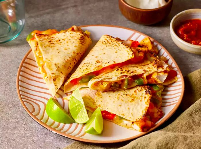 A chicken quesadilla, cut into quarters, served with salsa and sour cream on the side.