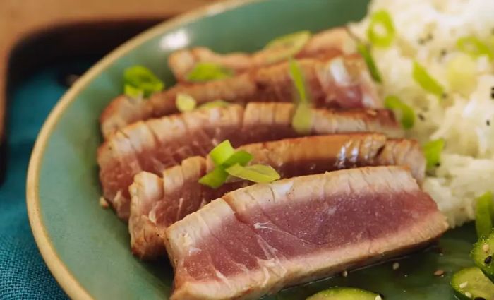 Seared Ahi Tuna Steaks served on a plate with green garnish, a side salad, and a portion of rice