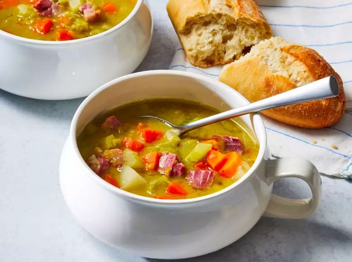 A bowl of split pea soup with a slice of bread in the background.