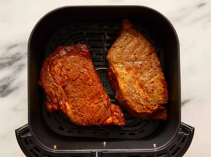 Top view of steaks cooking in an air fryer basket.