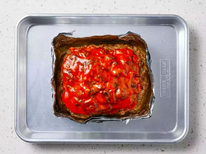 The topping is brushed over the meatloaf, which is then placed back in the oven to caramelize for 1 to 2 minutes.