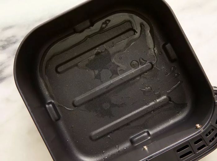 Overhead shot of an air fryer basket with water at the bottom.