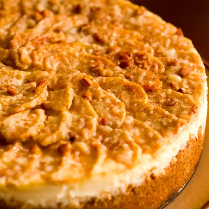 Close-up of a stunning apple cheesecake, with apple slices arranged in concentric circles, topped with cinnamon sugar and chopped pecans.