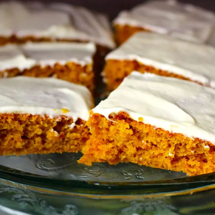 Pumpkin bars topped with icing, displayed on a glass cake stand.