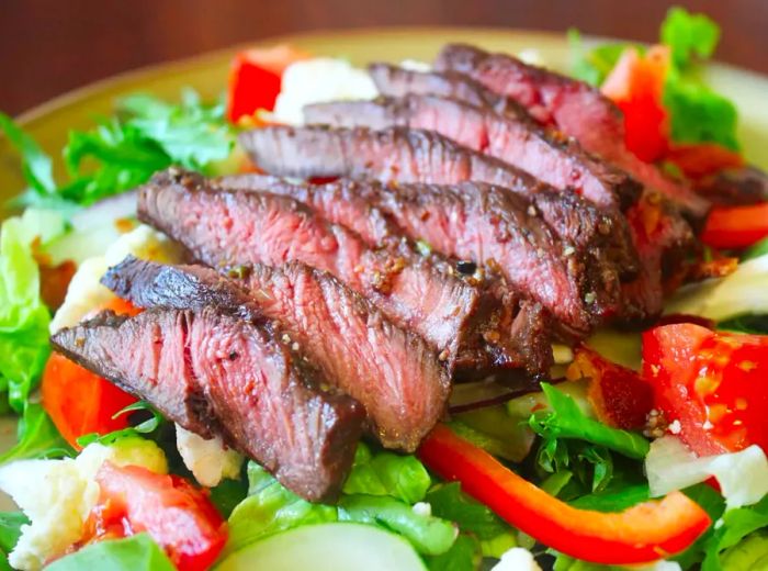 Close-up shot of sliced flat iron steak served over a fresh salad.