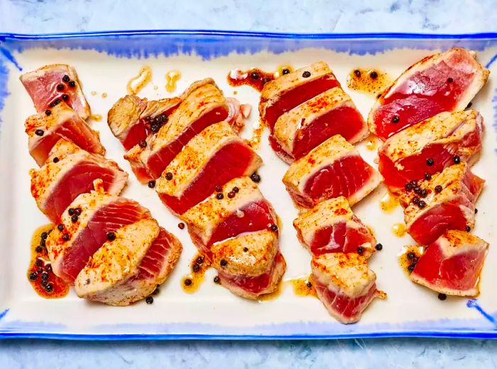 Several medium-rare seared tuna steaks neatly sliced on a blue and white platter.