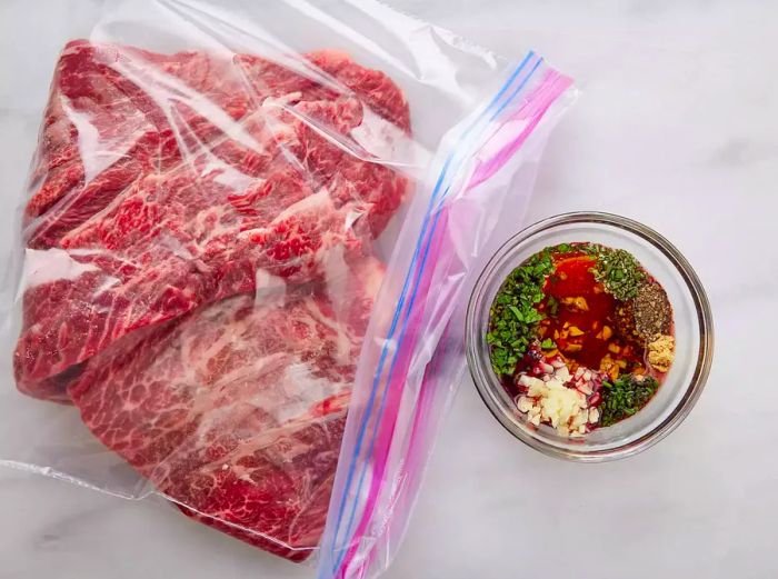 Bird's-eye view of the steak in a resealable plastic bag, next to a bowl containing the marinade ingredients.