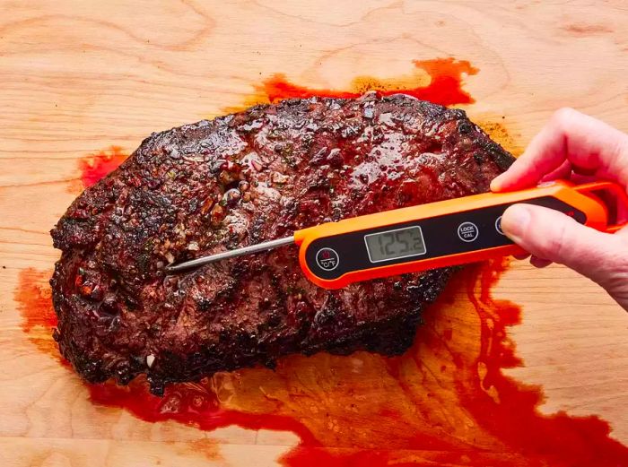 A high-angle view of a steak resting on a cutting board, with a thermometer inserted to check the internal temperature.