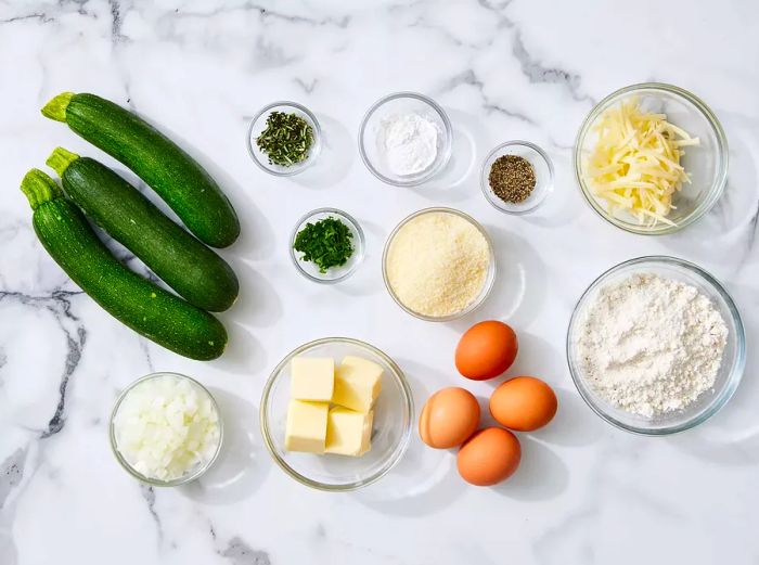 A top-down view showcasing all the ingredients for the zucchini pie neatly arranged on a marble countertop.